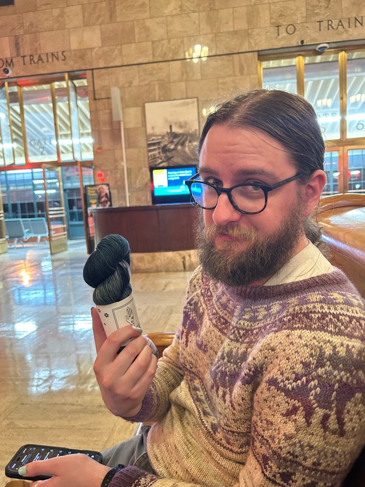 A man holding a skein of yarn in a train station.