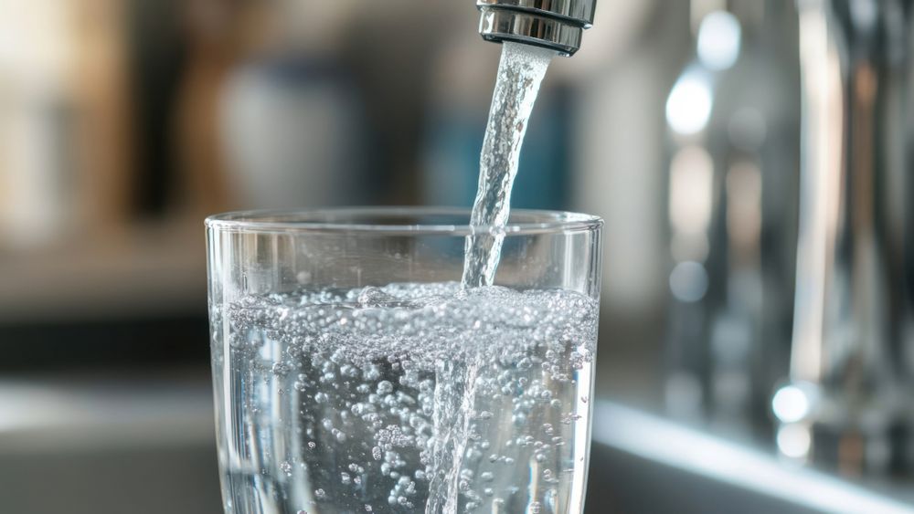 A faucet on a kitchen sink filling up a glass of water.