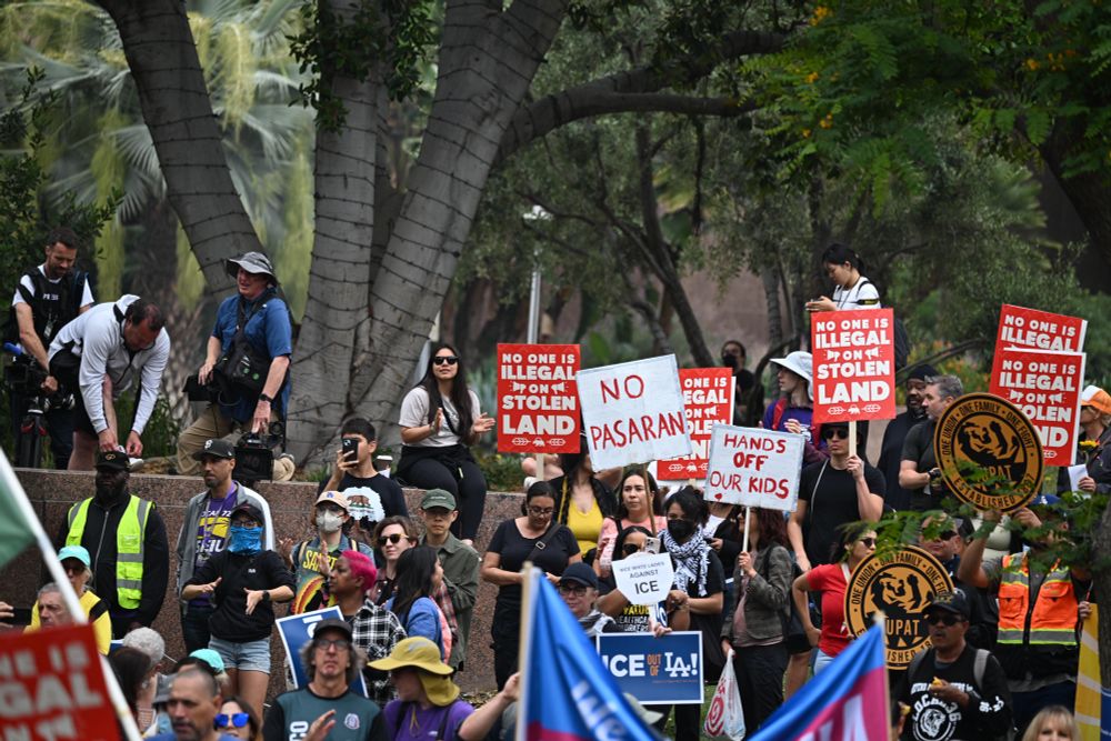 A crowded rally with attendees holding up signs that say no one is illegal on stolen land, hands off our kids, Ice out of LA.