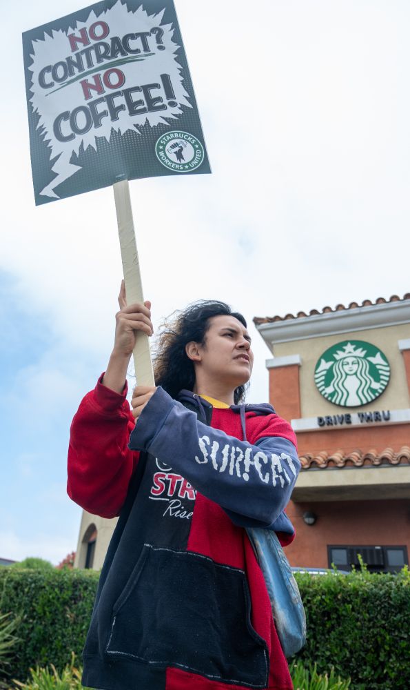 A supporter of Starbucks Workers United members outside a Starbucks with a No Contract, No Coffee sign
