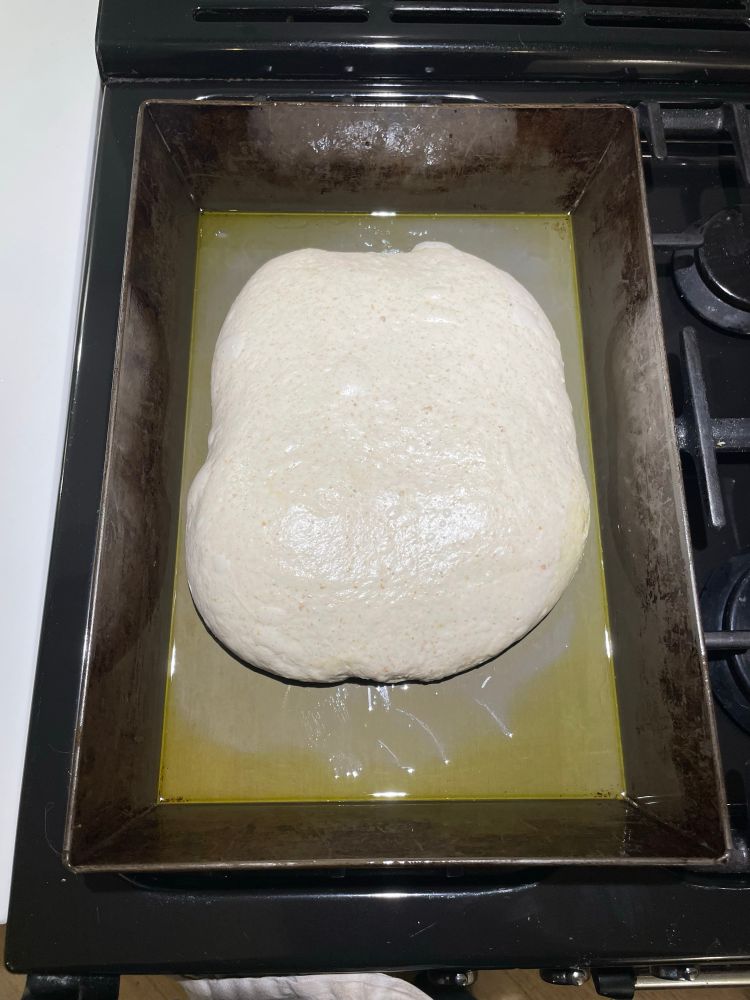 Bread dough in an oiled rectangular pan on a stovetop