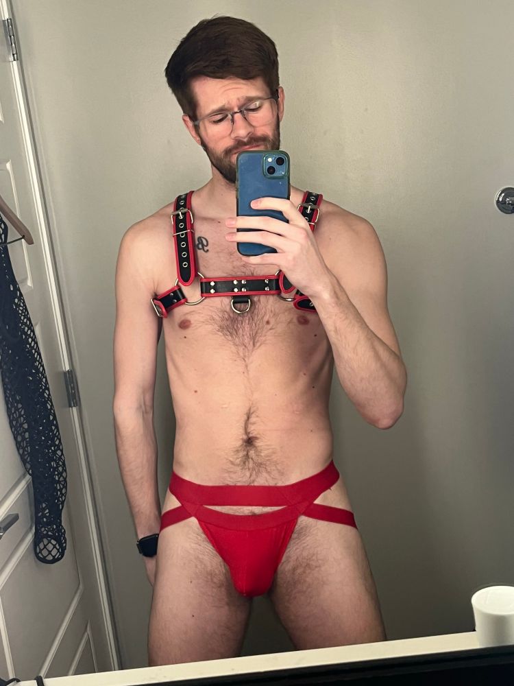 Gay mean wearing a red jockstrap and black harness with red accents 
