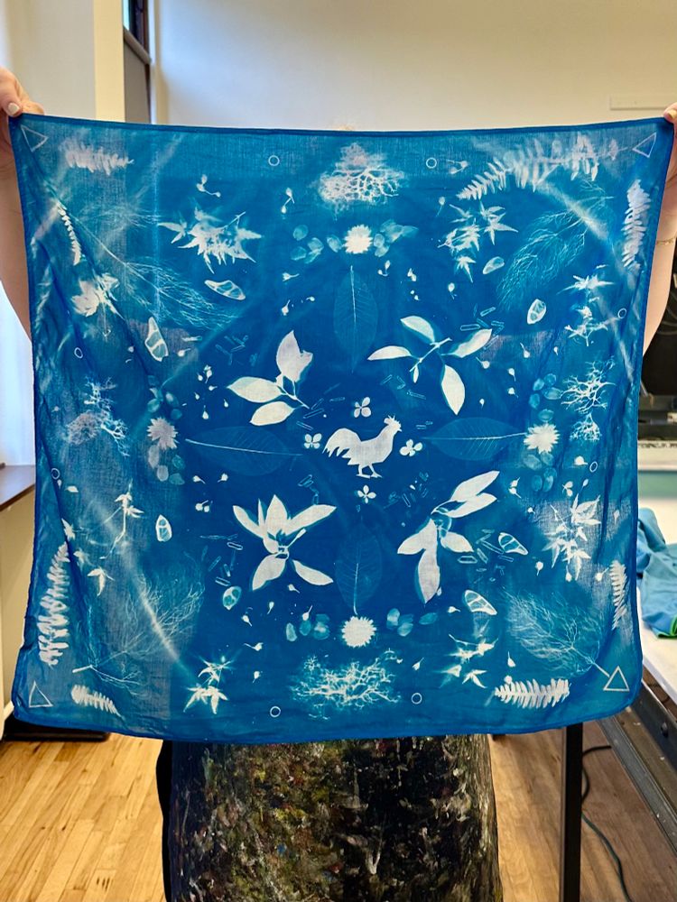 A cyanotype (blue and white) printed scarf with an intricate and complex pattern of flowers and leaves, and the silhouette of a chicken in the center