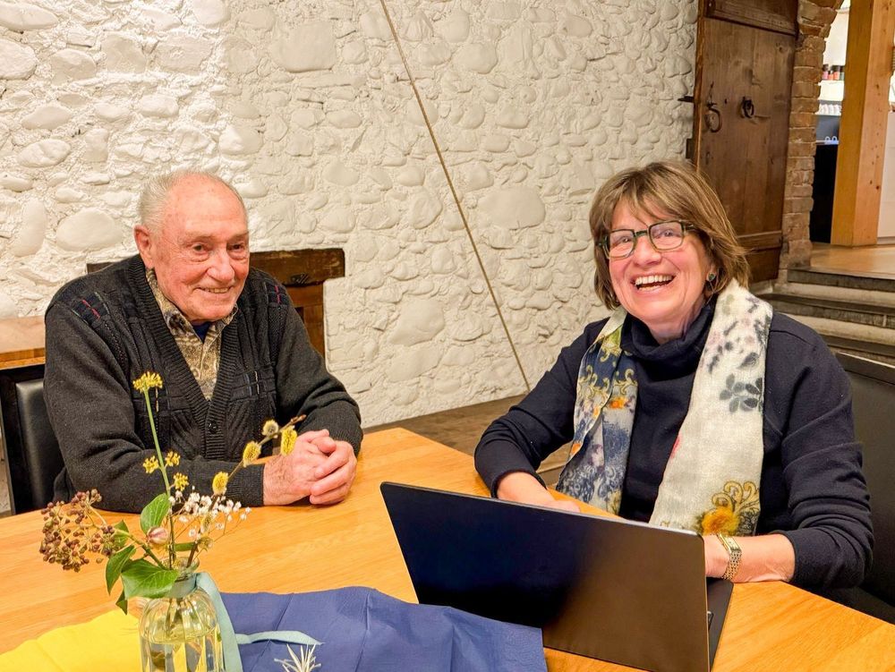 Auf dem Bild sind zwei ältere Menschen zu sehen: godi Brunner (etwas 90 Jahre alt) und Heidi Bühler (71 Jahre alt). Sie lächeln in die Kamera.