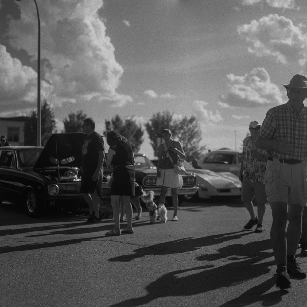 Black and white film photo of people walking around a car show.

Photo by Jacy Eberlein in St. Albert, Alberta in August 2025. Shot on a Hasselblad 500c/m with the 80mm Zeiss Planar f2.8 lens on Ilford Delta 100.