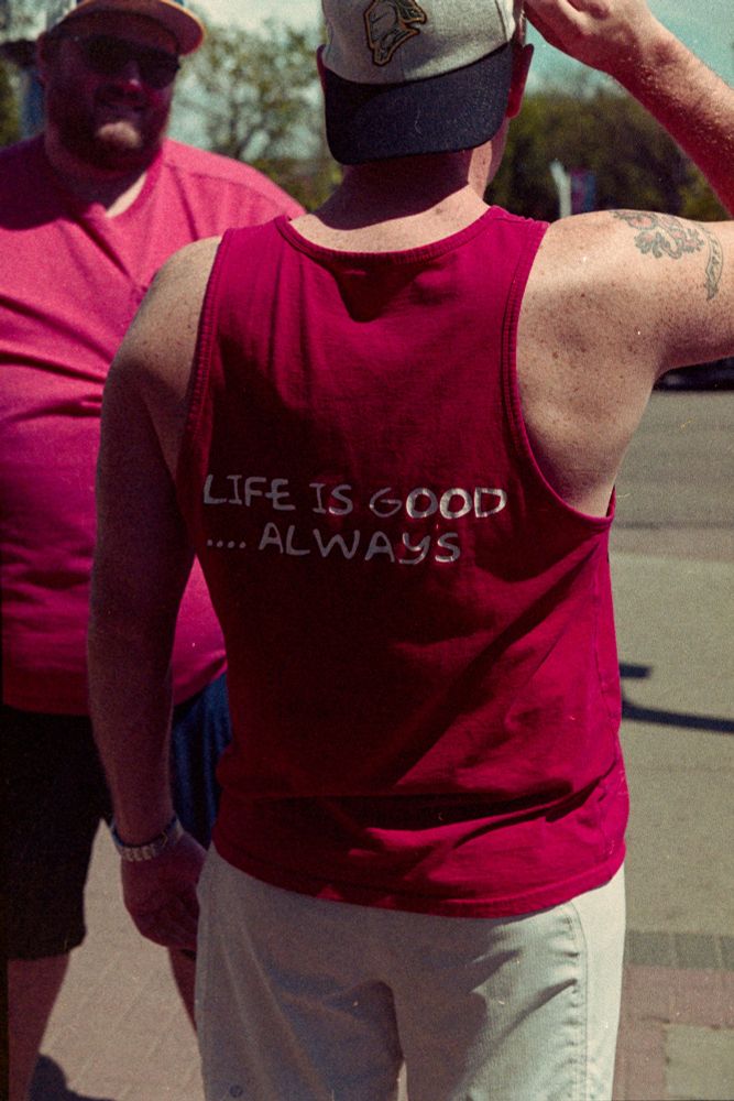 Colour film photo of a man with a red tank top from behind. His shirt reads "LIFE IS GOOD.... ALWAYS."

Photo by Jacy Eberlein, taken in Edmonton, Alberta on July 1st 2025. Taken with a Nikon F3 with the 50mm f1.4 AFD lens, and Kodak 400.