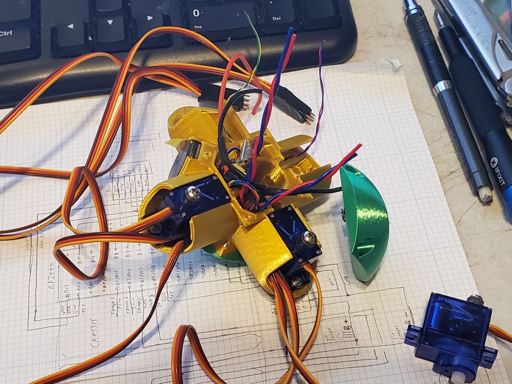 Part of a robot, a 3D printed object with wires sticking out of it at multiple angles as I try to fit everything where it's supposed to go.