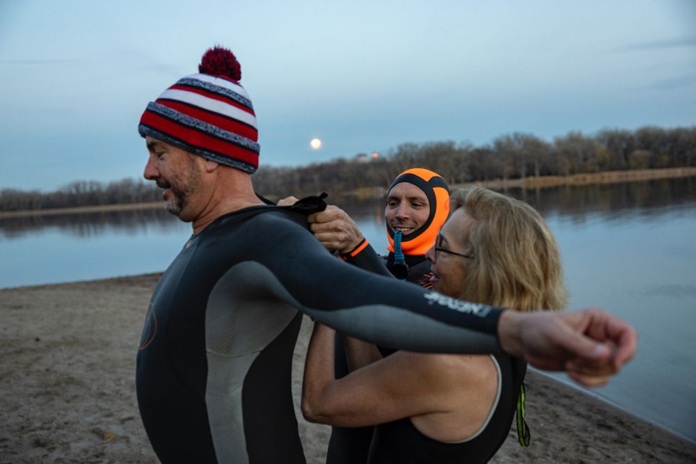Two people help someone get into a wetsuit at the shore of a lake. Photo by Ayrton Breckenridge/The Minnesota Star Tribune