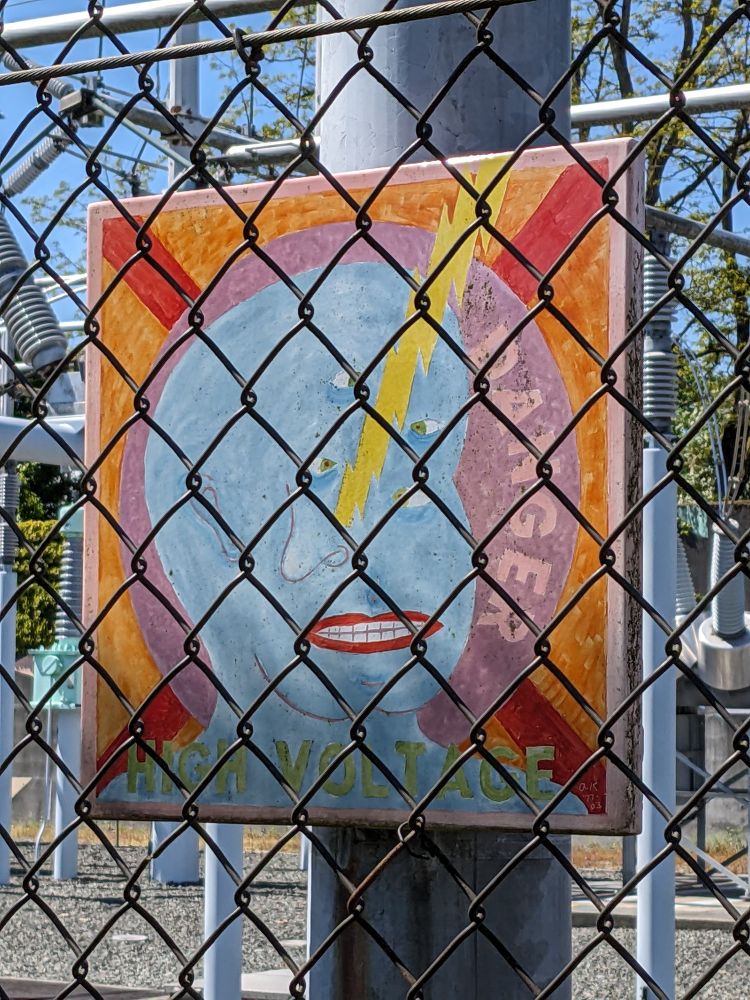 A danger high voltage sign with a three-eyed blue guy feeling the power. 