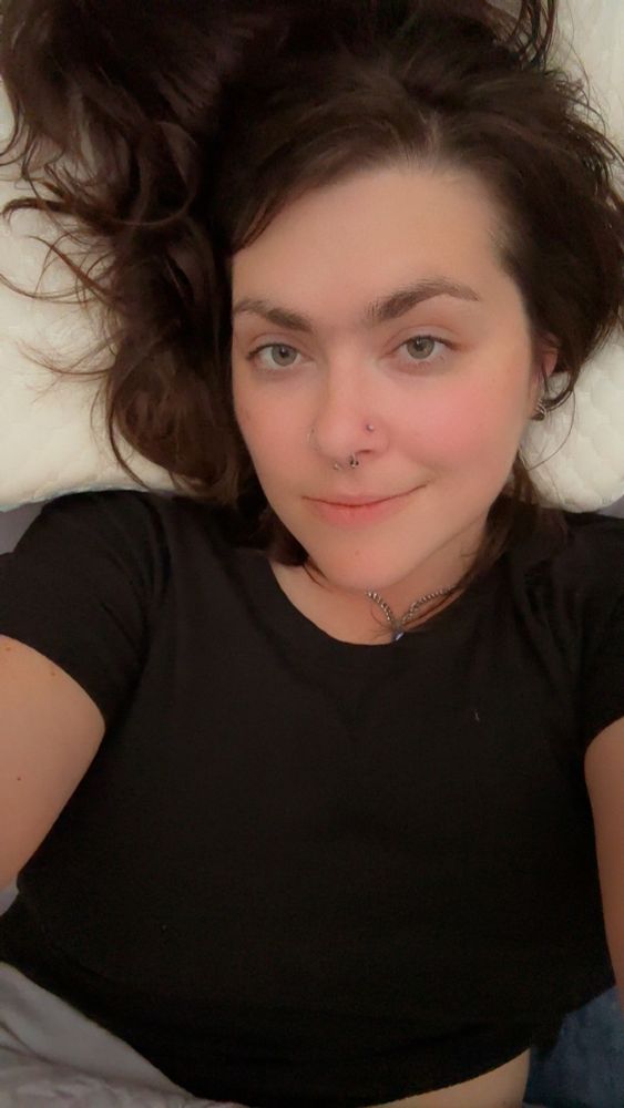 Stormy nightingale is laying on her bed wearing a black crop top and looking up at the camera 