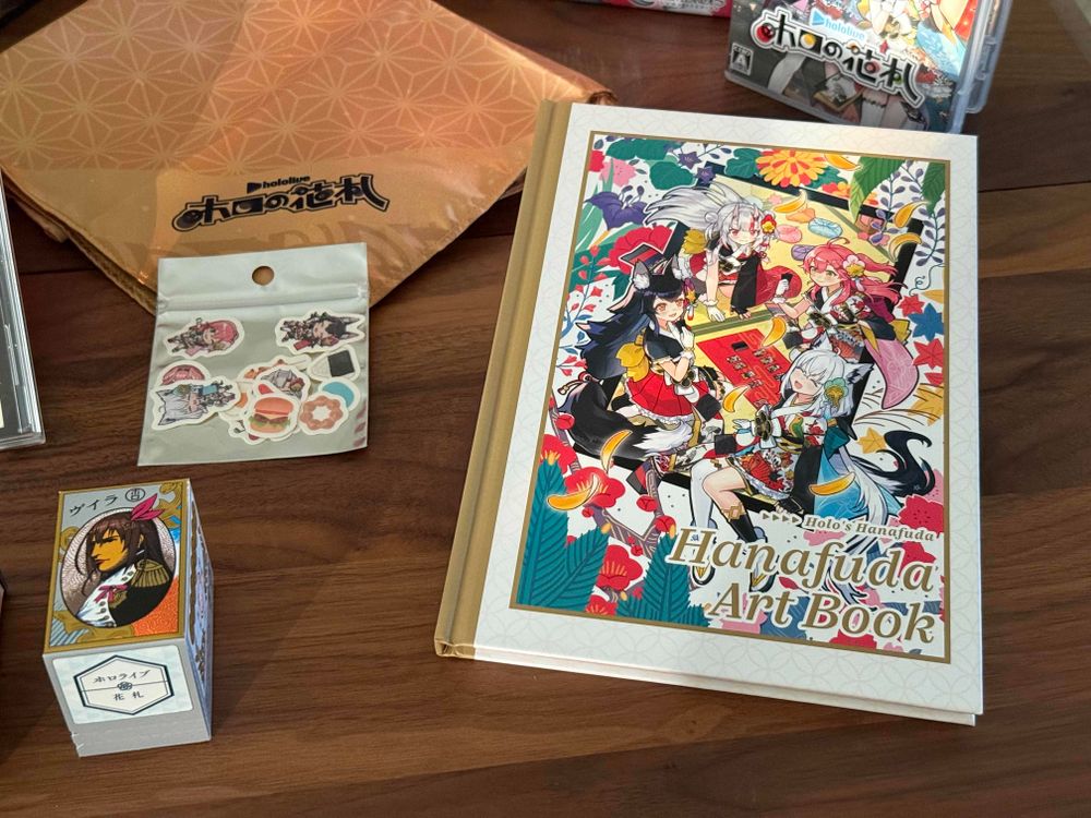 A closeup of the Hanafuda Art Book, with the art from the box on the front. The deck of cards is also shown, wrapped with art of the Nintendo Napoleon hanafuda deck, but with Tokino Sora’s bow and hair accessory in his hair. 