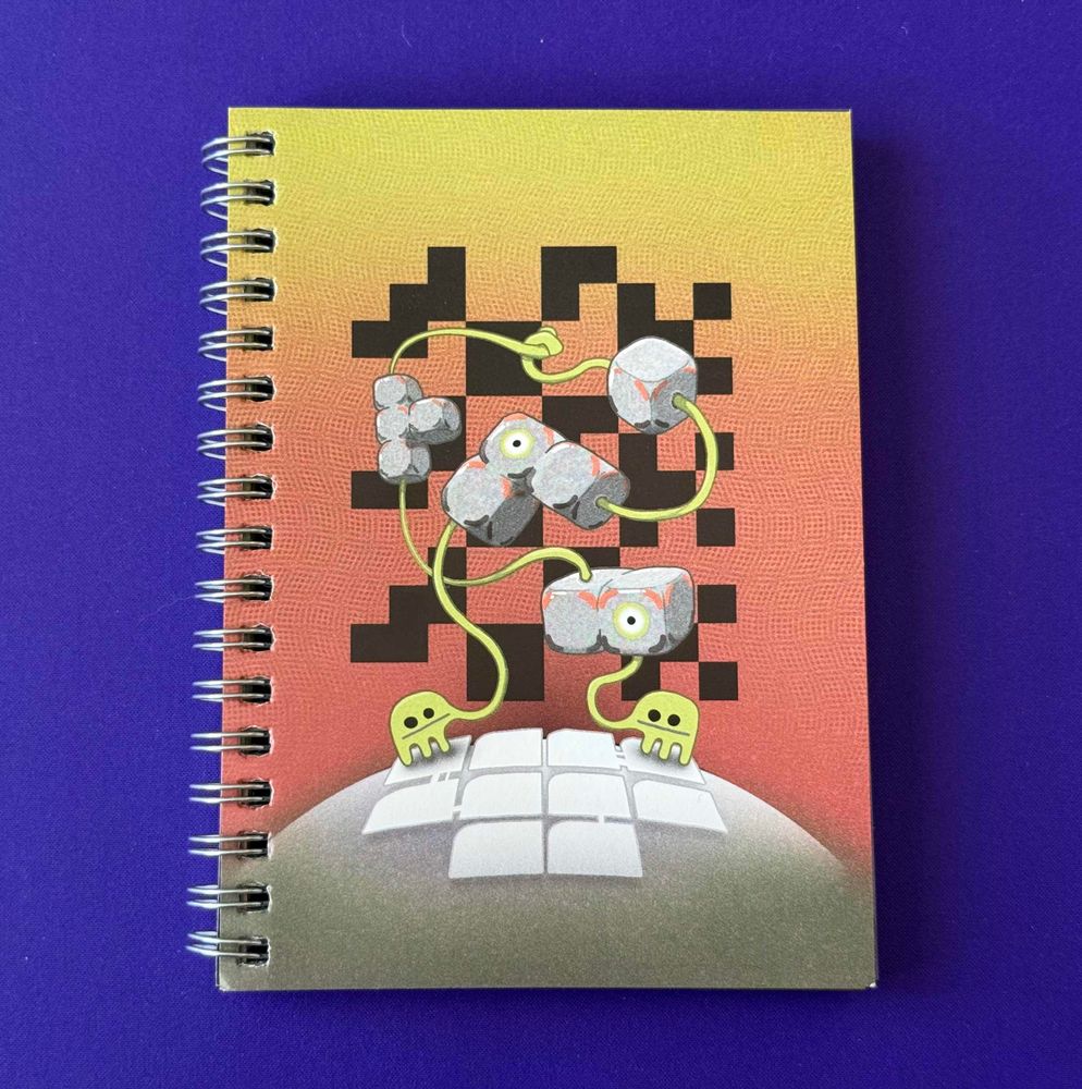 Workworkwork, a small spiral-bound book. The cover features small green creatures holding stone-colored blocks in polyomino shapes. The title is written in a large pixel grid in the background of the image. 