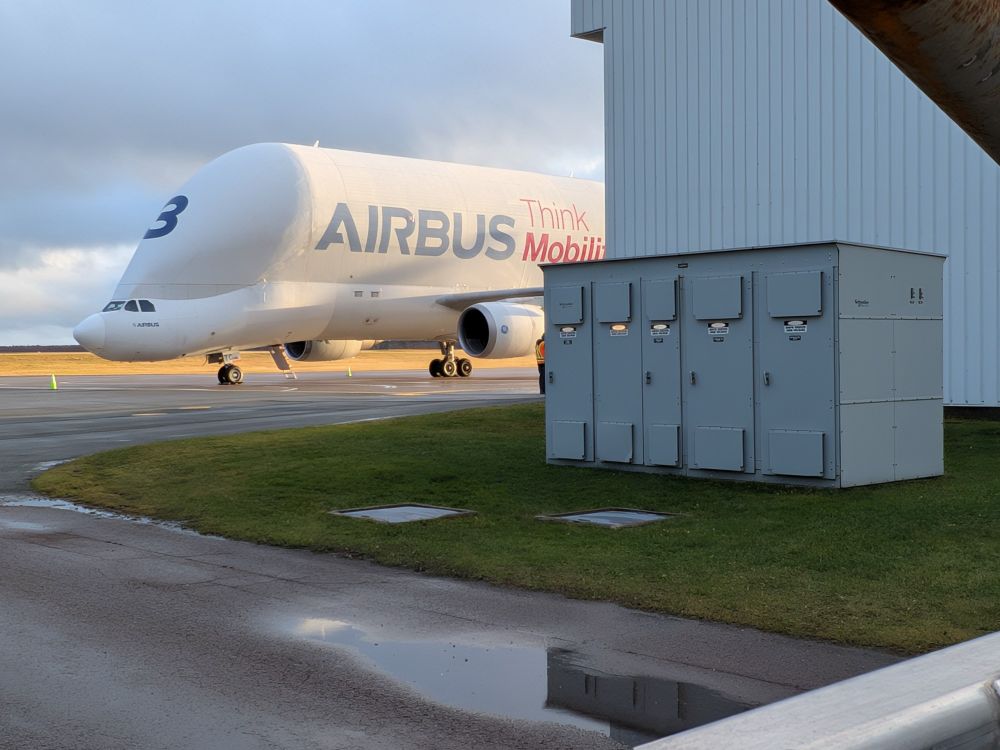 Front left side view of an Airbus beluga A300-600ST super transporter. The rear part of the plane is obscured by a building. The identifier '3' is visible on the front of the aircraft.