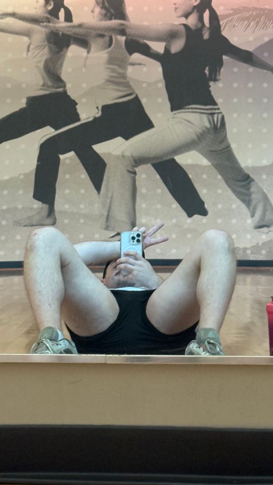 Me on my back with my phone covering my face holding a peace sign up between my legs.