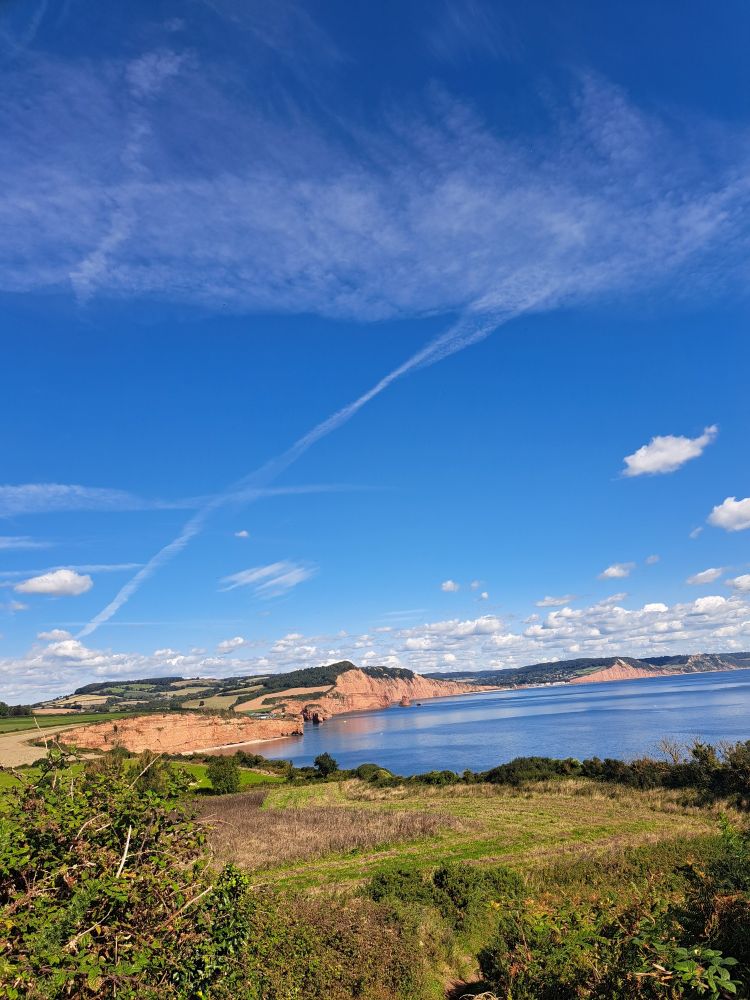 South West Coast Path, looking east towards Peak Hill from ~2km easy of Budleigh Salterton. Blue sky with contrails, blue sea, red cliffs