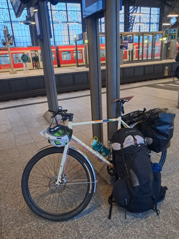 Bicycle with loaded panniers and a large backpack rested on it. On a train platform.