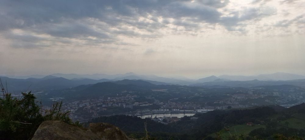 Paysage basque. Des collines en plusieurs rangées se perdant dans l'horizon. Une ville en contrebas.