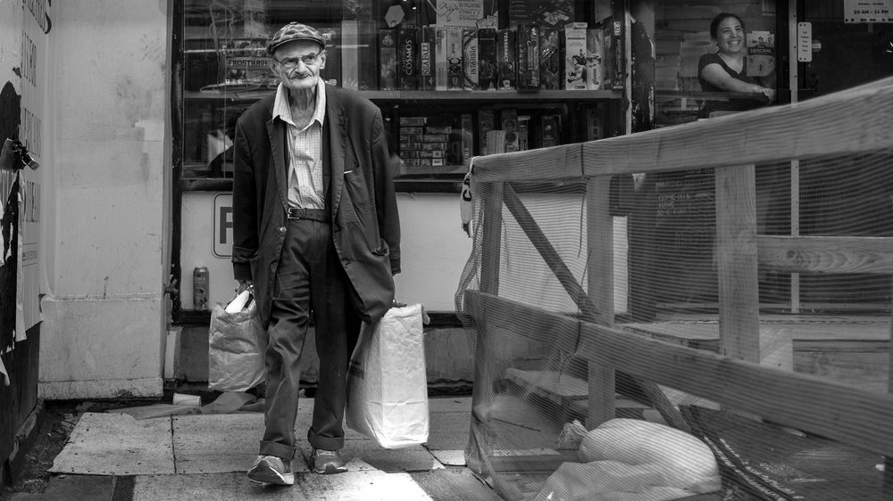 Black and white candid photo of older man walking towards the camera with a scowl on his face 