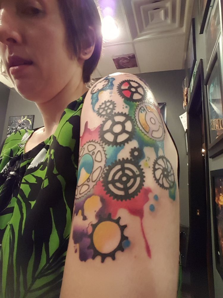 A tattoo on my shoulder/upper arm, bike gears/cogs with brightly colored water color splotches behind them
