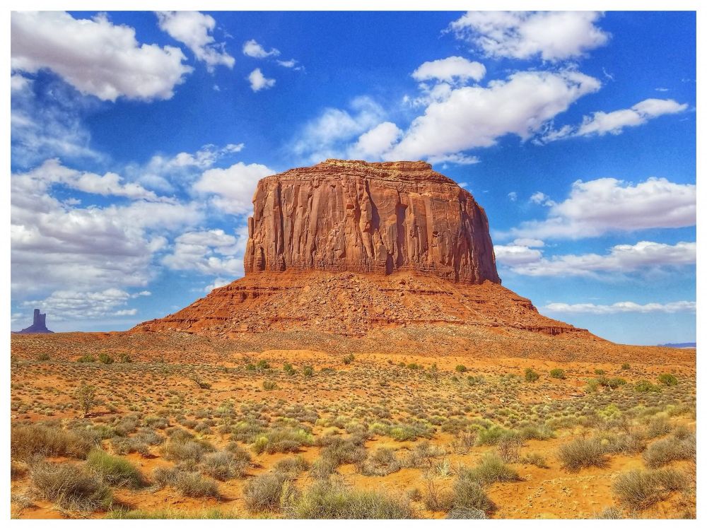 A huge stone monolith in Monument Valley in the American Southwest. Desert is all around along with a beautiful blue sky with lovely white clouds. 