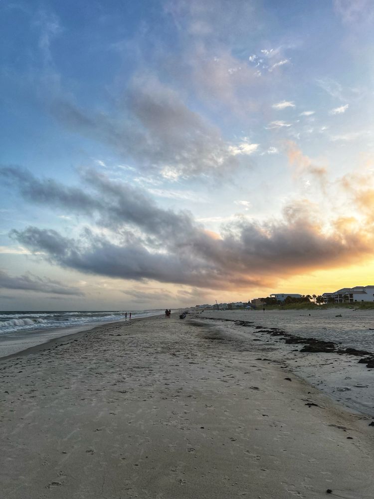 A long short of a sandy beach right at sunset. The Gulf of Mexico is to the left. A beautiful cloud hovers in the sky.