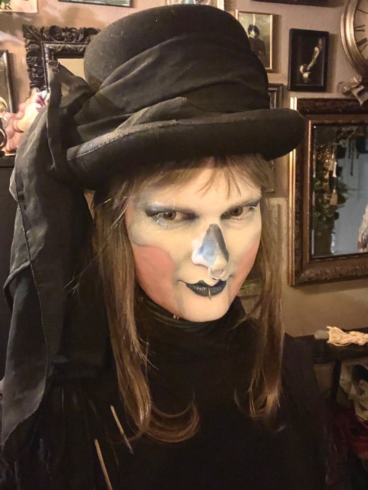 Selfie of myself with vague skeleton face makeup and a black dress and hat with a big shawl around it 