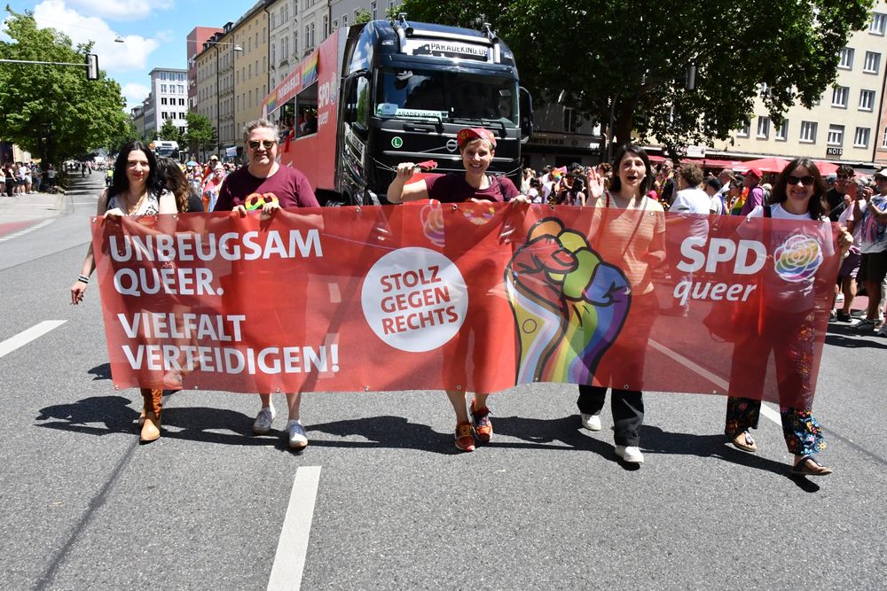 Eine Gruppe von fünf Personen hält ein großes rotes Banner mit der Aufschrift „Unbeugsam queer. Vielfalt verteidigen! Stolz gegen rechts.“ Dahinter fährt der SPDqueer-Truck. Die Menschen wirken entschlossen und fröhlich.