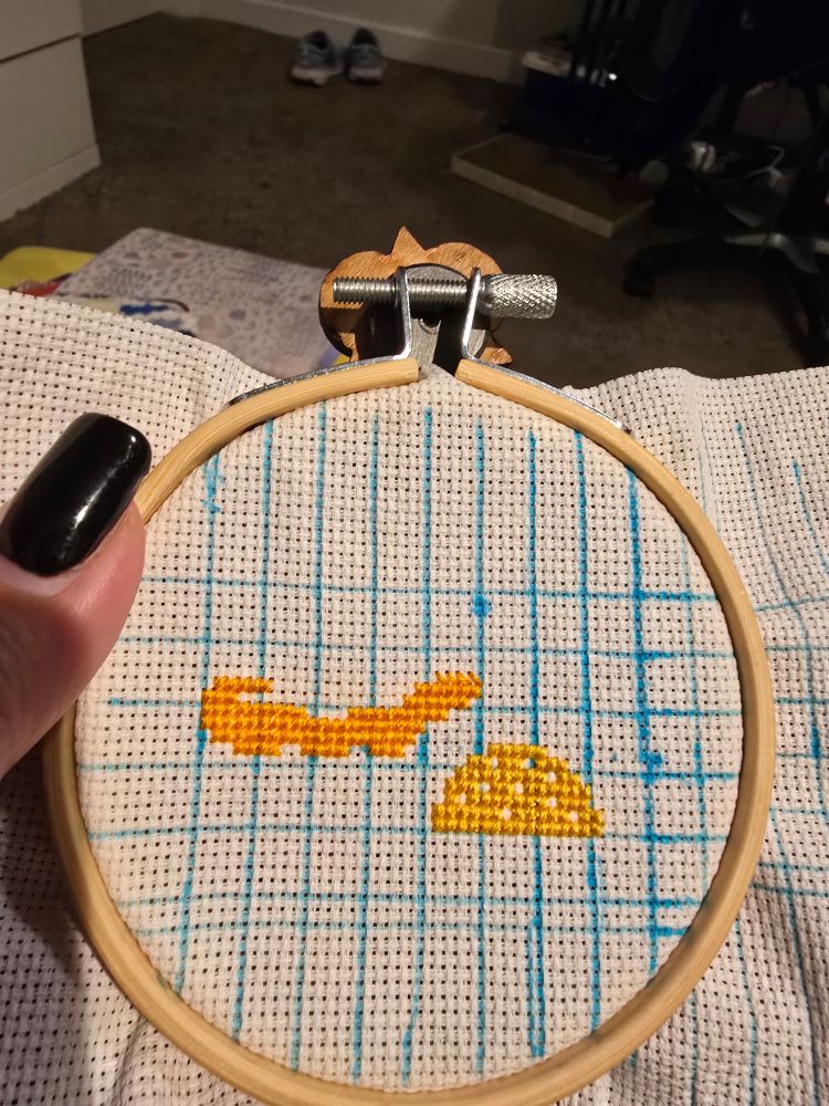 white aida with a blue grid. there is a golden top of a button mushroom and the beginning of the top of a golden chanterelle mushroom.