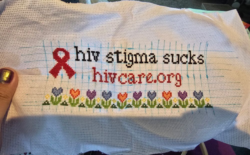 blue grid on white aida. there is a red ribbon with the statement 