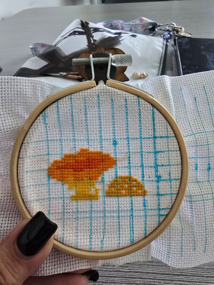 white aida with a blue grid. the complete tops of a golden button and golden chanterelle mushroom is at the center of the bamboo hoop.