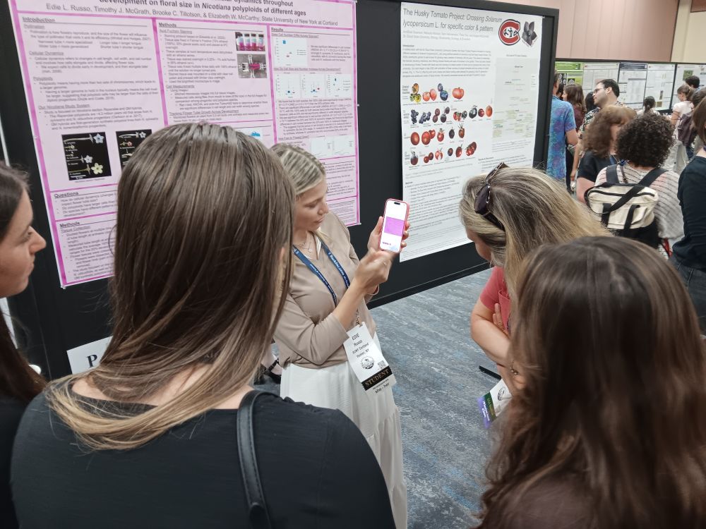 Undergrad woman scientist showing supplemental pictures on her phone to present her poster to a crowd