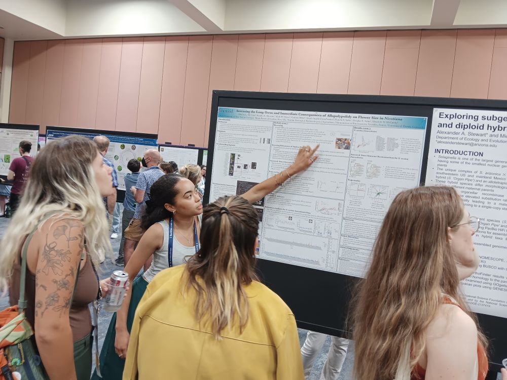 Undergrad woman scientist pointing to her poster as she presents it to a crowd