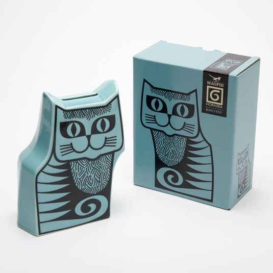 A cat moneybox in a 70s-feeling Hornsea pottery style, teal pottery in the shape of a cat, with the cat drawn on the front face with black lines. The big-eyed cat is smiling dumbly but winningly. The moneybox is on the left and its box is on the right, with a picture of the moneybox on it.