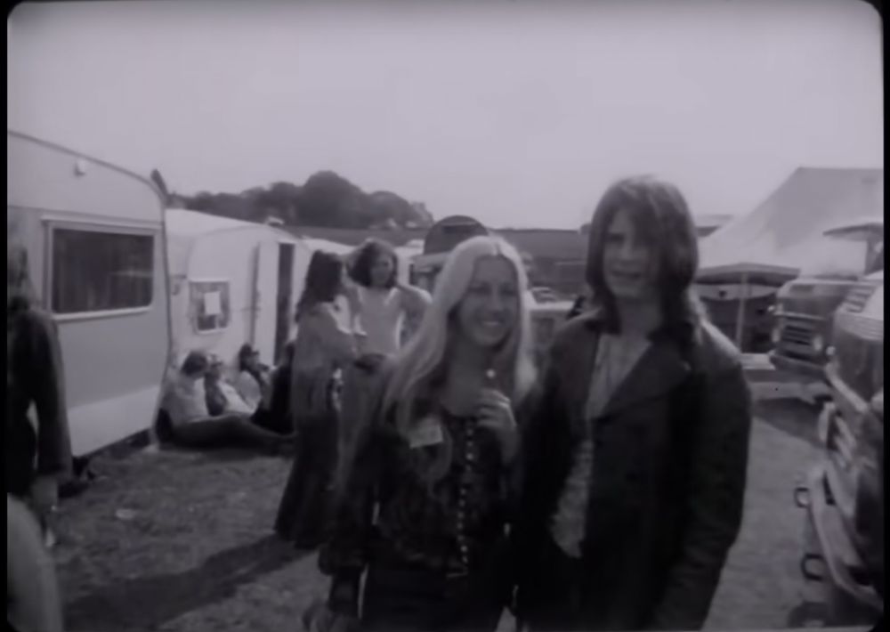 Black and white screenshot of Ozzy Osborne and unidentified blonde woman backstage at the Hollywood Festival, England, in May of 1970