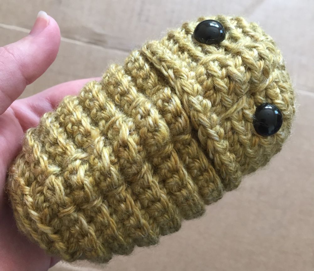 Crochet trilobite with black plastic safety eyes. Yarn is a golden yellow giving it an especially phallic appearance.