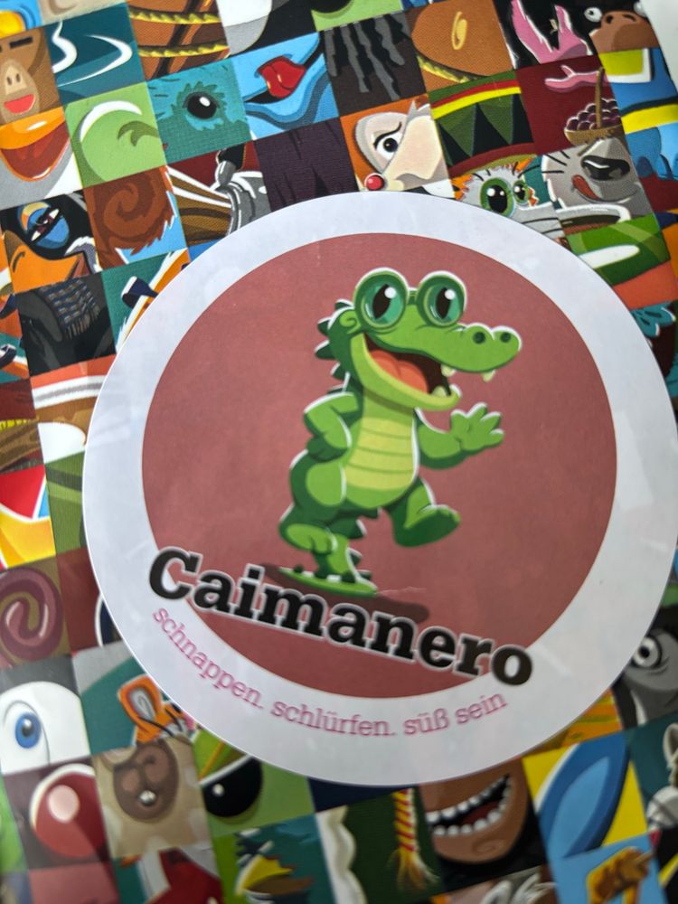 Zu sehen ist die Nahaufnahme einer Kaffeetüte mit einem niedlichen Grünen Comic-Kaiman und der Aufschrift "Caimanero - Schnappen. Schlürfen. Süß sein"