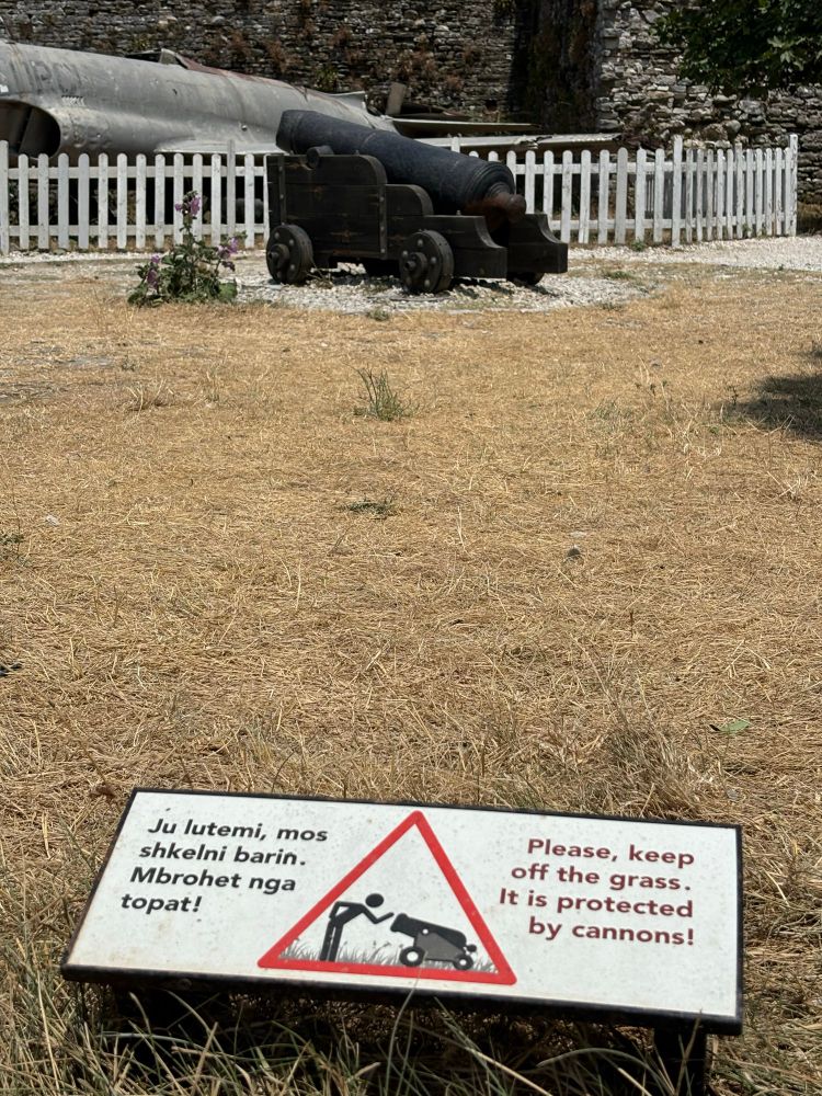 Eine Kanone auf einem sehr vertrockneten Rasen mit einem Warnschild “Please keep of the grass. It is protected by cannons!”