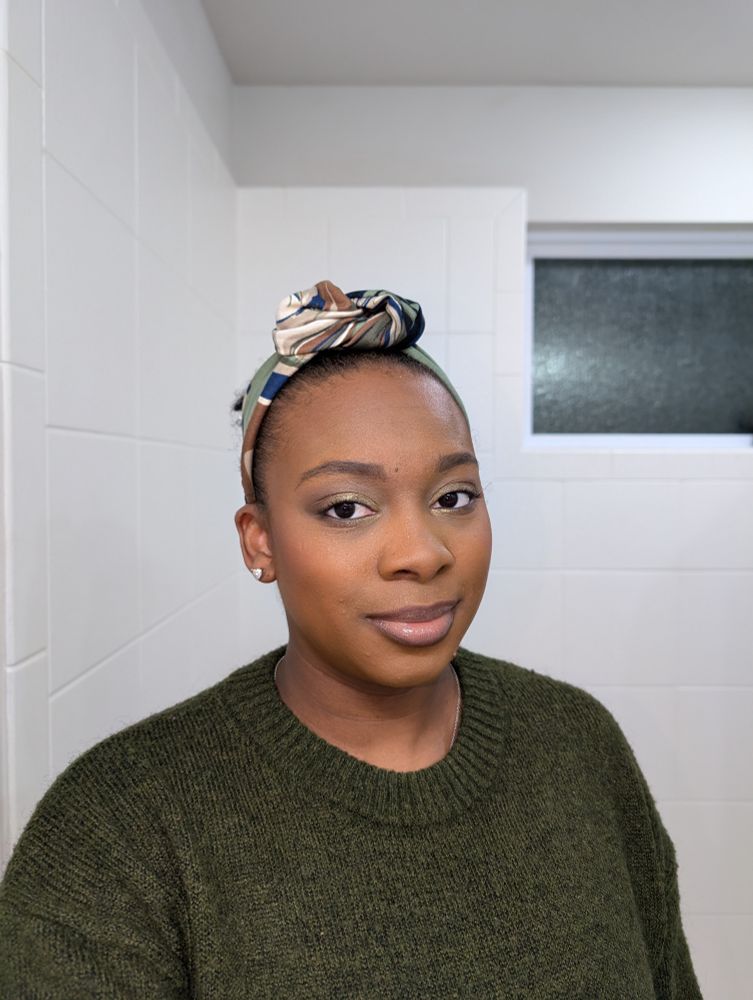 A Black woman wearing a forest green sweater and headband with navy, beige, brown and olive green swirls 