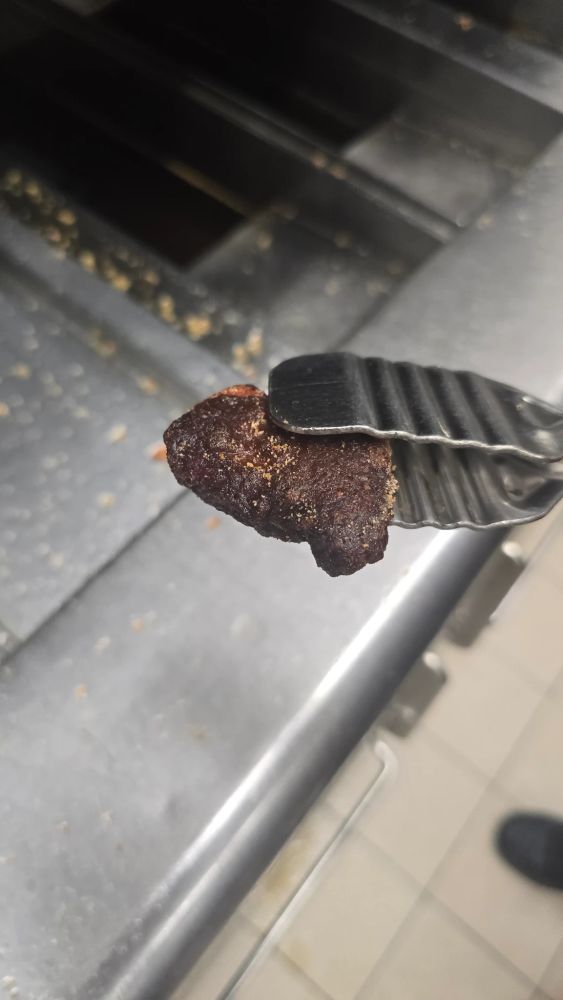 A McDonalds chicken nugget being held in tongs over a fryer. It's completely burnt