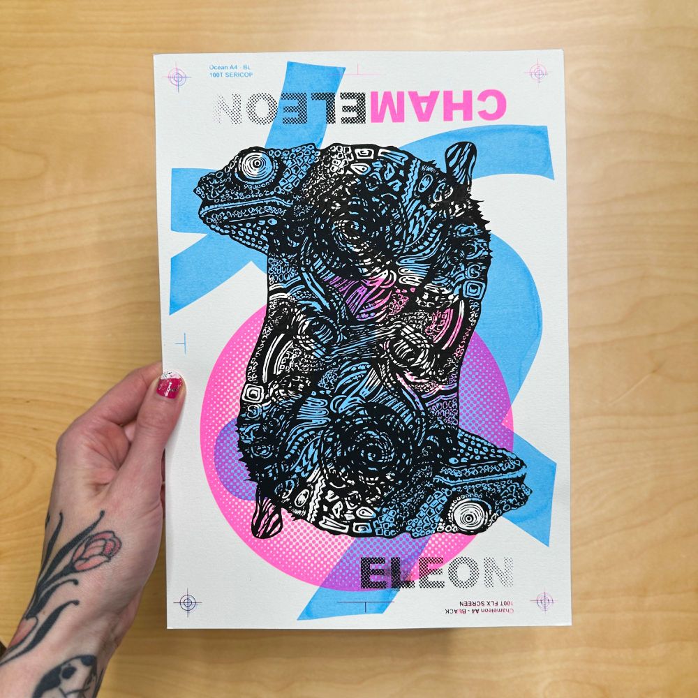 hand hält einen testprint (monoprint) siebdruck. mehrer farb und motiv schichten sind hier übereinander gerdruckt. Ein Chamäleon  in schwarz doppelt übereinandergedruckt und abstrakte Formen in Neon Pink und Hellblau im Hintergrund