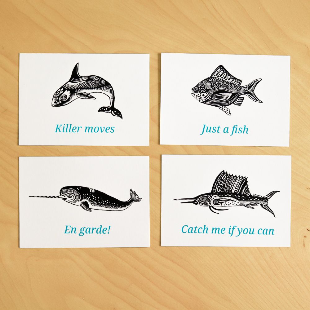 4x A6 mini screen prints with fish & whale illustrations on a table. Orca "killer moves", Fish "just a fish", Narwhal "En garde!, Sailfish "Catch me if you can"