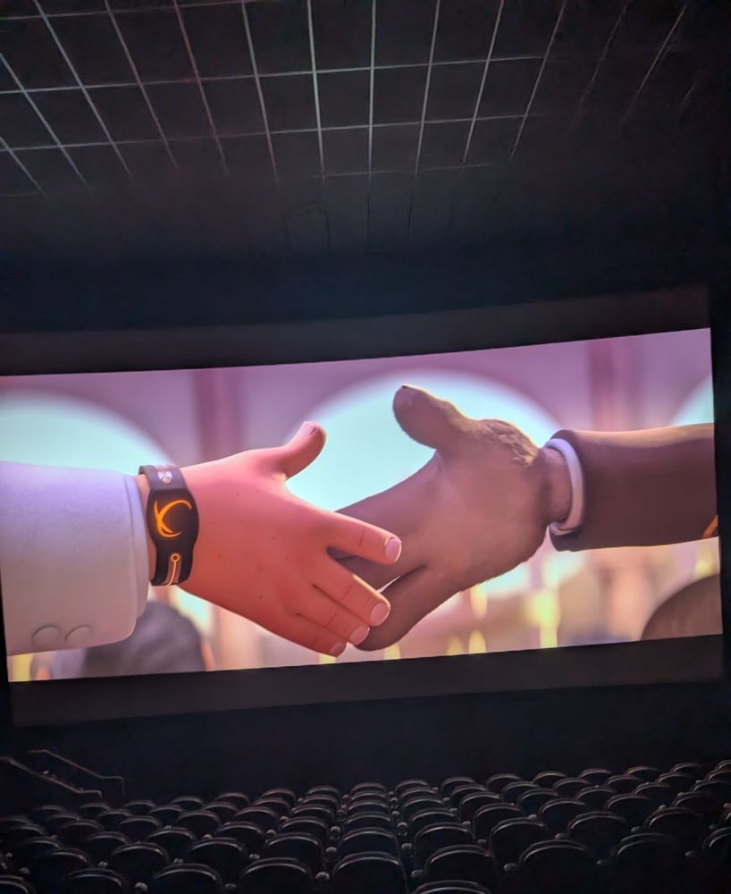 A picture of OtterlyNoah attending the animated film The Bad Guys 2 in theaters, where Mr Wolf is shaking hands with an Elon Musk knock off who has a watch that is meant to resemble SpaceX