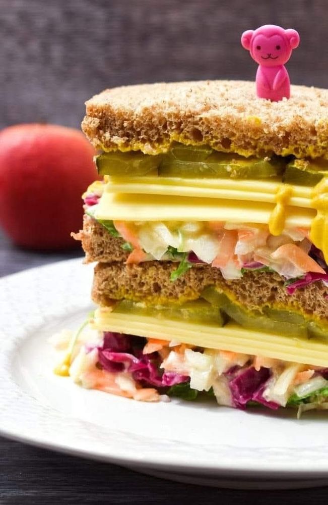 A vegan New York Deli Sandwich stacked on a plate looking delicious, topped with a cute pink monkey sandwich pick.