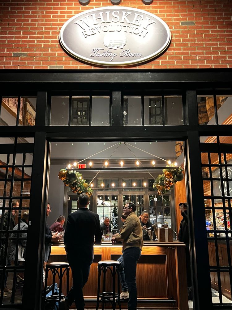 Shot of the whiskey resolution door. People are hanging at the bar and it looks like a brick building with a large bar in center and holiday decor above 
