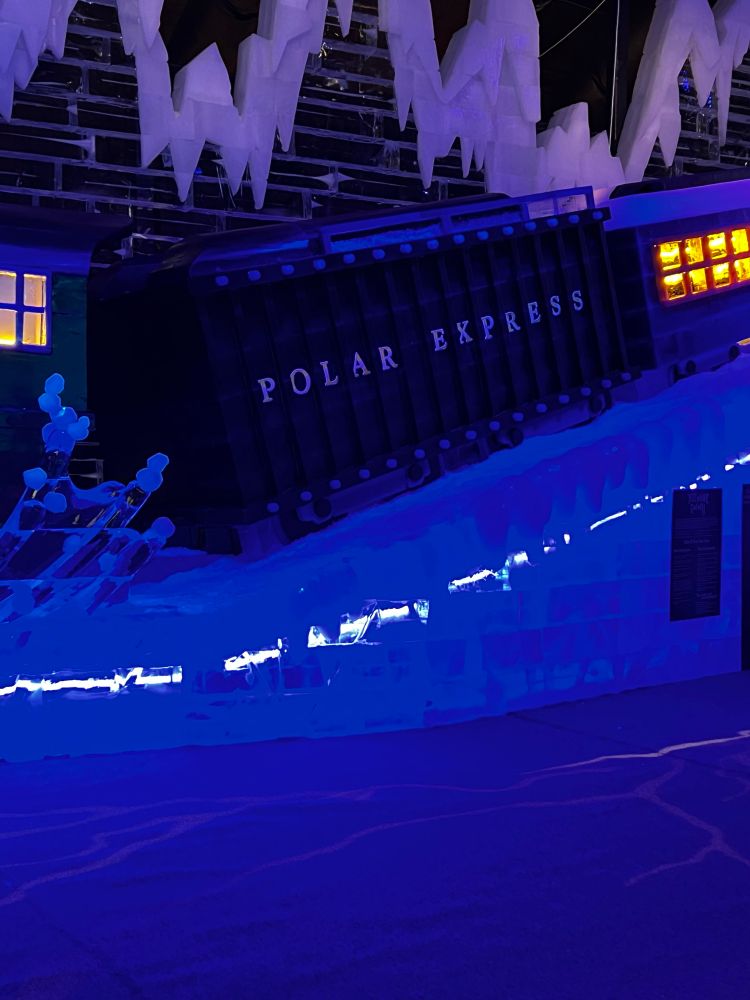 Ice sculpture of the polar express train with some dark cars and some lit up on a snowy hill. 