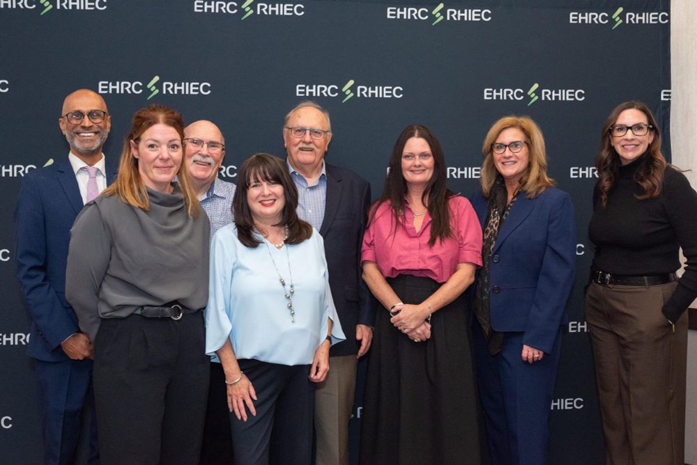 Group of eight professionals smiling for a photo in front of a backdrop with multiple "EHRC" logos.