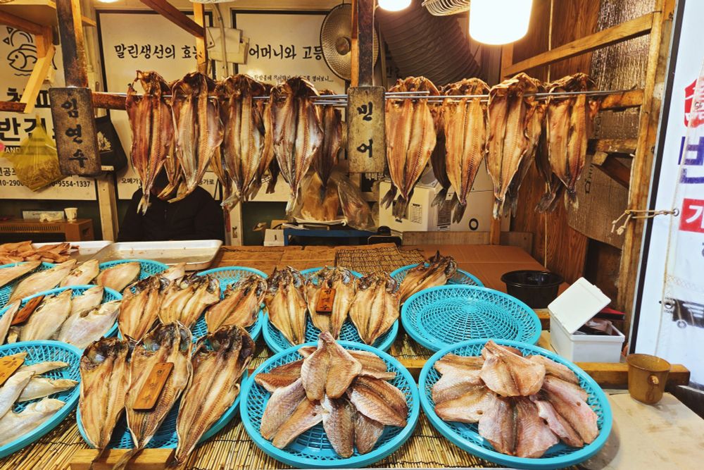 A dried and smoked fish stand. Some fish are hanging, the others displayed on teal mesh platters