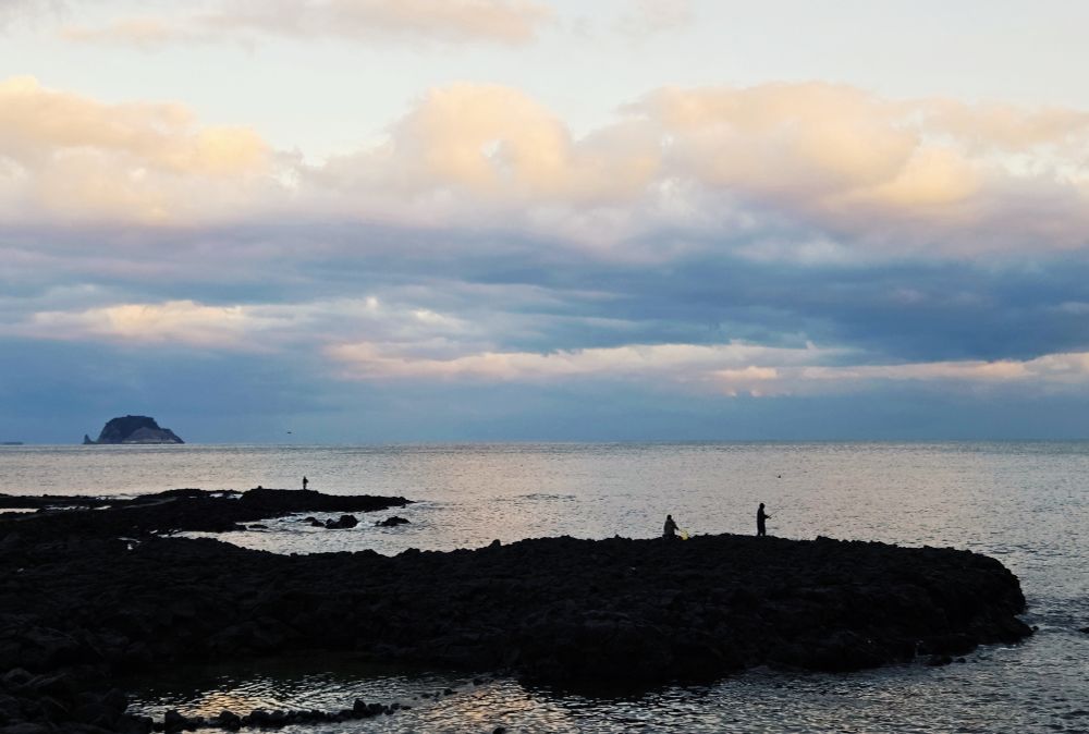 Three fishers on black rock near sunset