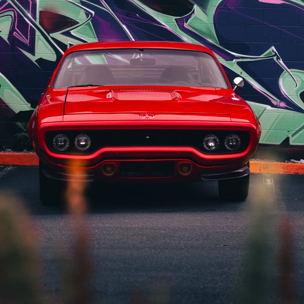 Classic red Plymouth with a murals in the background. 