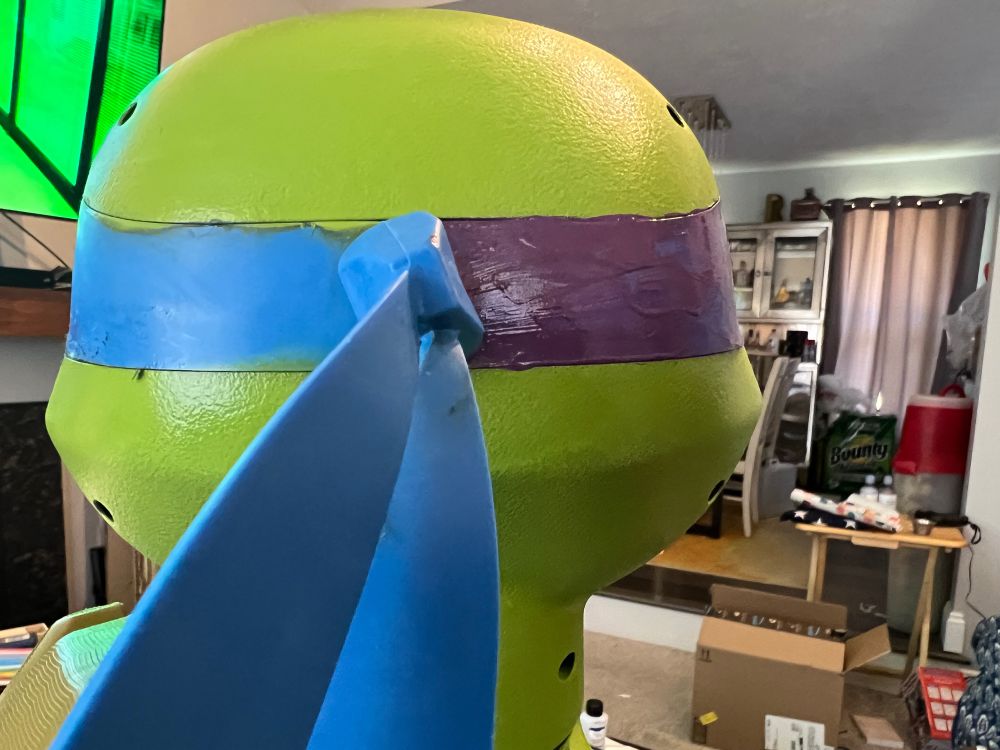 Back of a Ninja Turtle’s head. The blue bandanna is painted purple on the right side of the image. The layer of purple is uneven with bits of blue poking through.